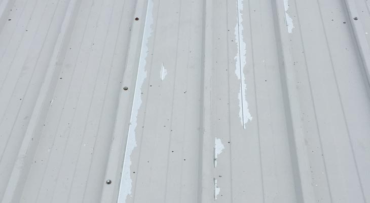 Industrial roofing jet wash reveals delaminating offset white plastisol