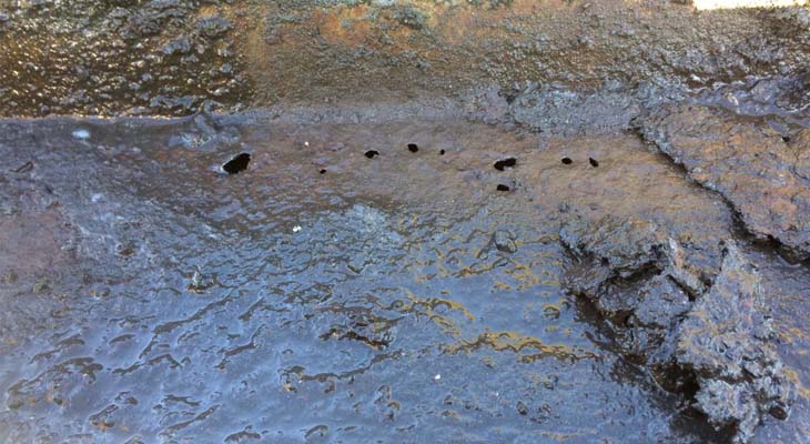 Heavily corroded industrial gutter with pitted holes