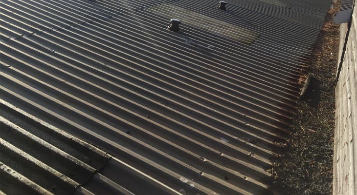 Old dented industrial roof with gutter debris build up